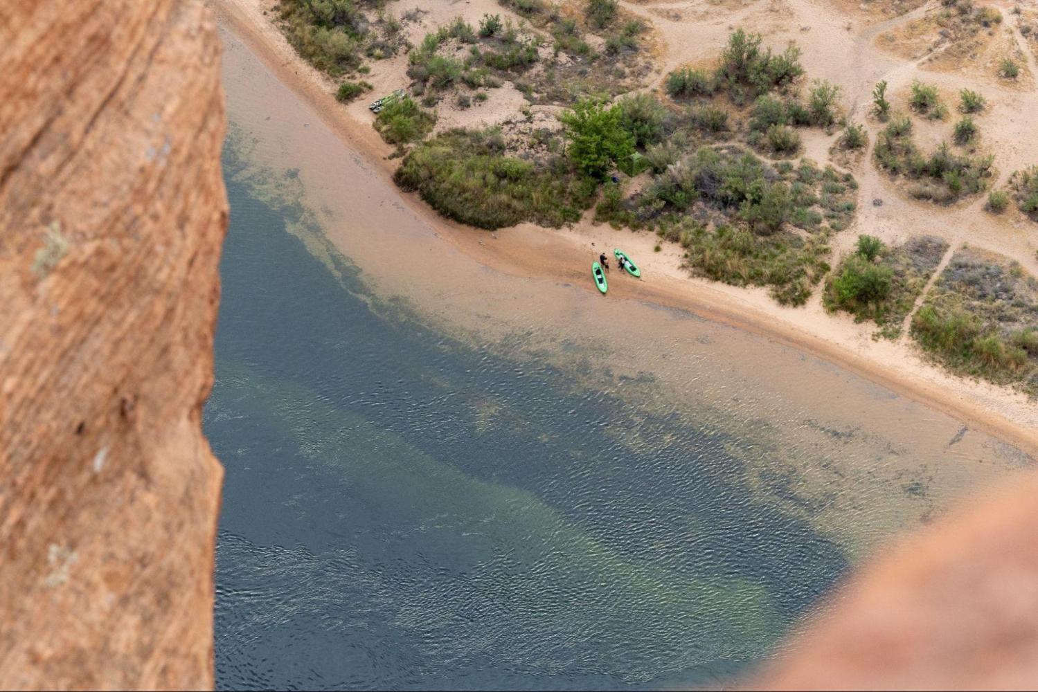Aerial view of kayaks on riverbank surrounded by desert terrain.