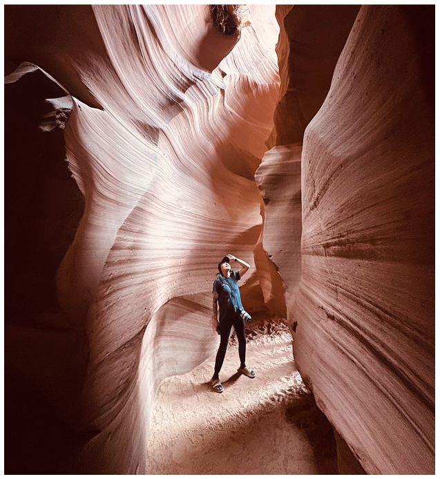 Person stands in narrow canyon with textured sandstone walls.