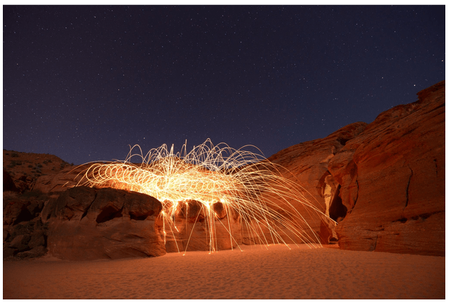 Long exposure of red canyon with light trails under starry night sky.