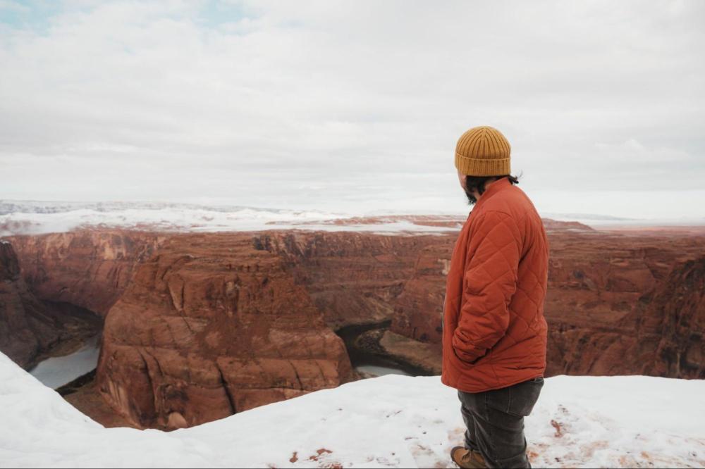 Person in a red jacket and yellow beanie overlooks snowy canyon.