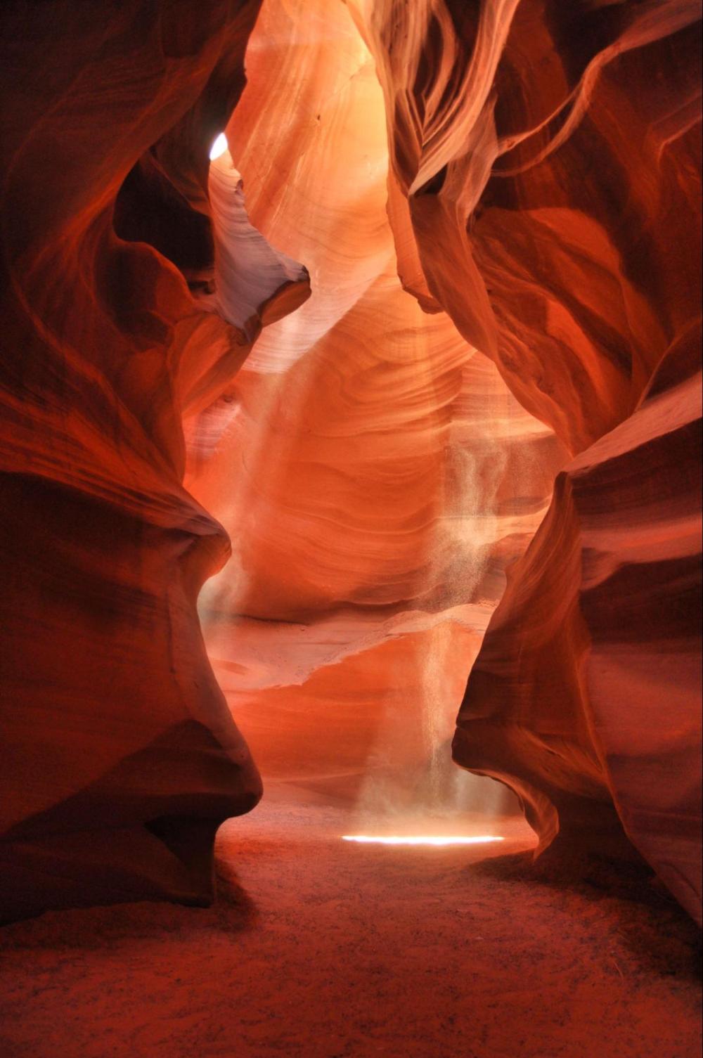 Sunlight streams through narrow sandstone canyon walls, illuminating the red-orange rock formations.