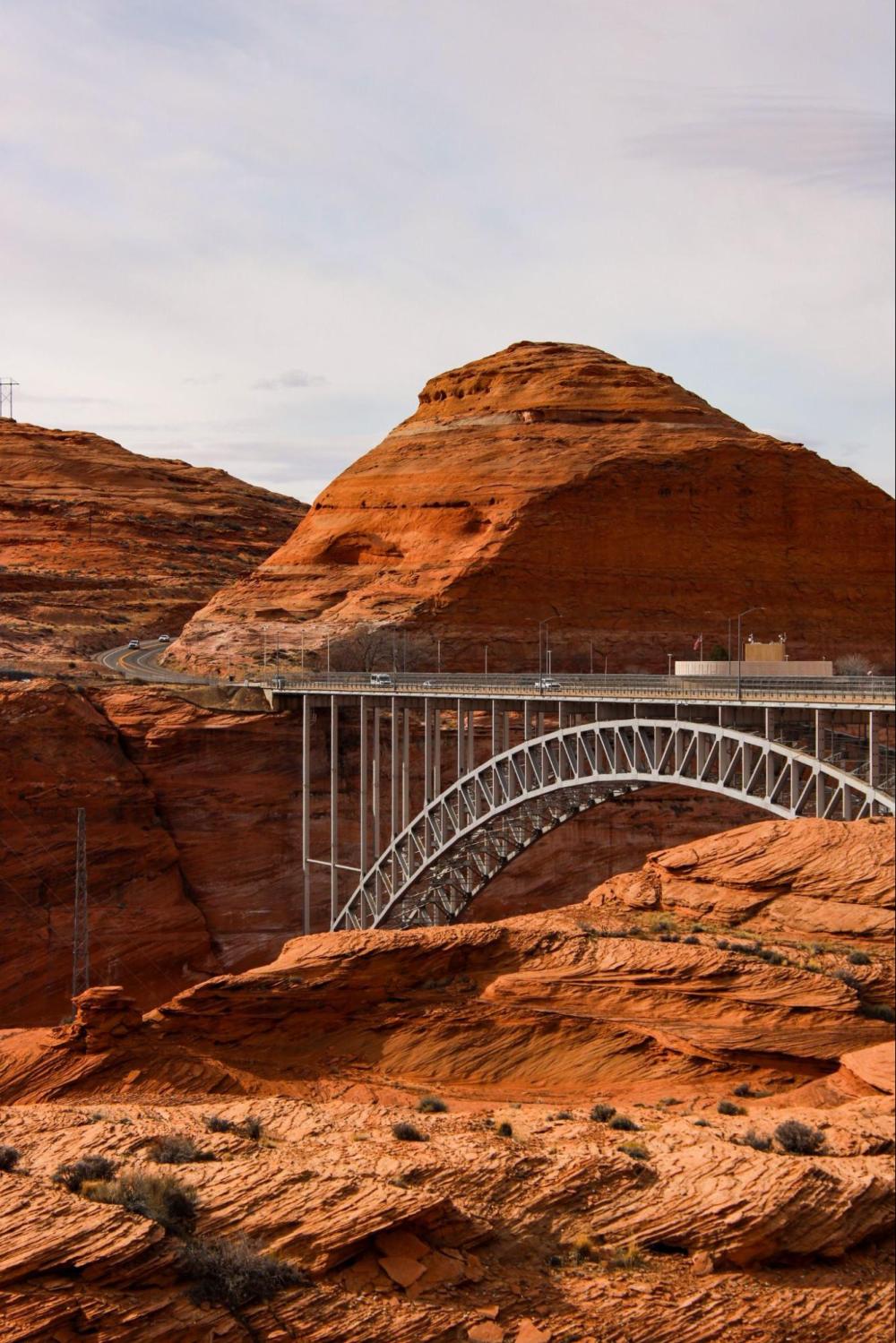 Steel arch bridge over canyon with red rock formations in the background.