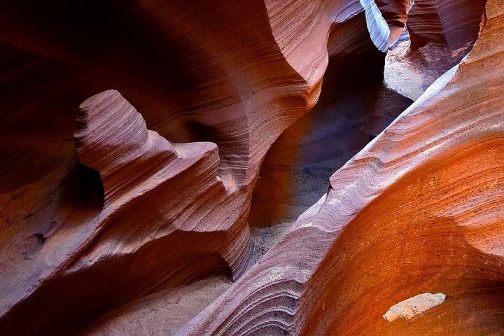 Sunlight illuminating curving, textured sandstone walls in a narrow canyon.
