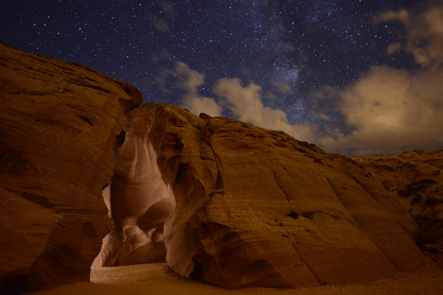 Starry night sky over a glowing canyon entrance with rock formations.